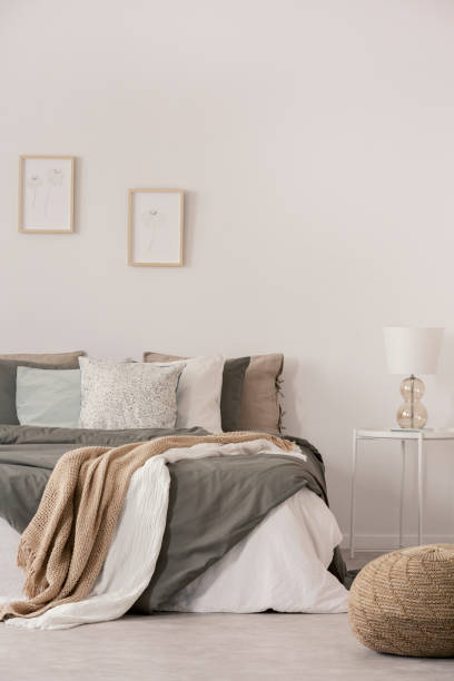 istock Stylish white lamp on simple nightstand table next to warm bed with cozy grey bedding 1165921526