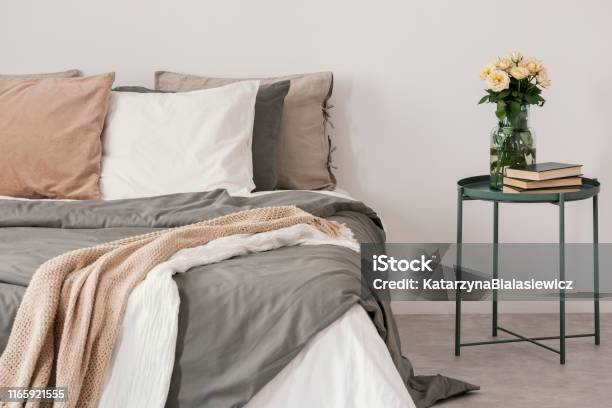 White Roses In Glass Vase And Books On Stylish Nightstand Next To Big Bed With Linen Pillows And Cozy Blanket Stock Photo - Download Image Now