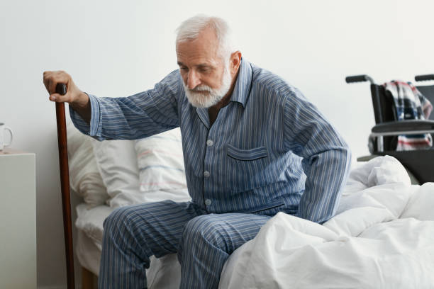 Sad senior man with Alzheimer's disease holding walking stick and sitting on his bed in nursing home Sad senior man with Alzheimer's disease holding walking stick and sitting on his bed in nursing home old man pajamas photos stock pictures, royalty-free photos & images