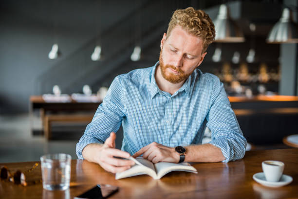 istock Young man reading a book in a coffee shop. 1165925891