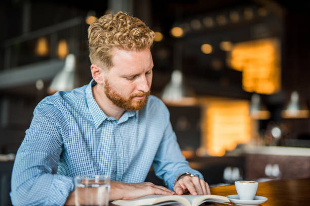 istock Handsome man reading a book in a coffee shop. 1165926065