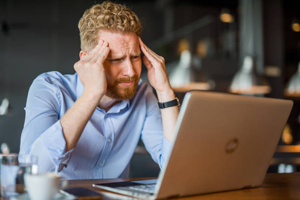 istock Frustrated young man having a headache while looking at laptop in coffee shop. 1165926104