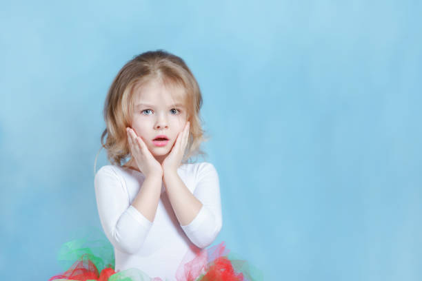 schöne kleine mädchen ballerina in bunten tutu. blonde blaue augen kind tragen schöne ballett rock auf neutralen hintergrund. modell posing express überrascht emotion. kid halten hände auf gesicht - ballet dress studio shot costume stock-fotos und bilder