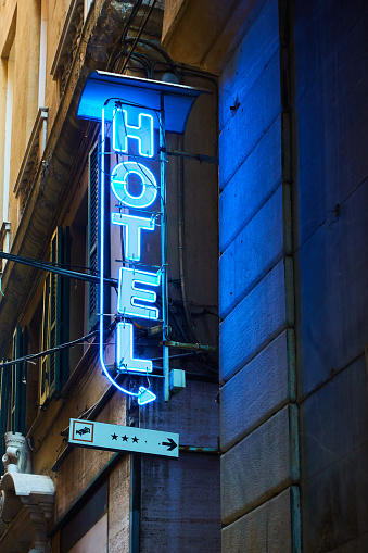 Blue neon hotel sign with arrow on the wall close-up