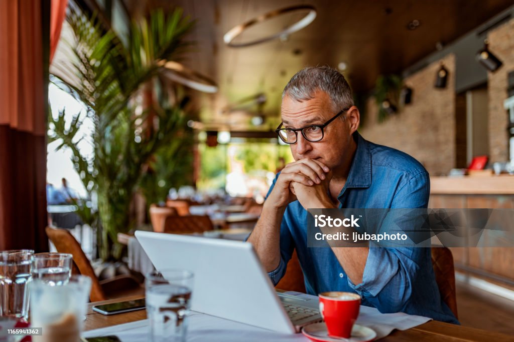 Sometimes the stress is just too much Contemplating businessman in the restaurant feeling sad. Full concentration on work. Confident mature man working on laptop while sitting at his working place in office. Tired manager sitting in restaurant surrounded with coffee and laptop computer having tired look , having pain, being sleepy and exhausted. Tiredness. Men Stock Photo