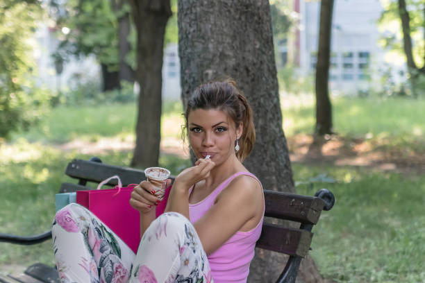 istock Beautiful Young Woman Eats Ice Cream in a Public Park. 1165942318