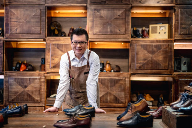 Confident Male Taiwanese Shoe Store Owner Successful male Taiwanese merchant leaning on a display table featuring high quality dress shoes for men. lace up stock pictures, royalty-free photos & images