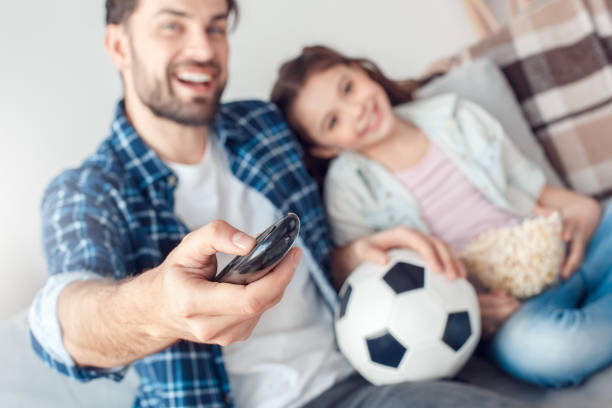 istock Father and little daughter at home sitting man holding remote controller switching channels happy close-up 1165956303