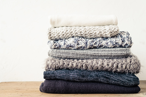 Pile of knitted woolen sweaters. Monochrome gradient shades grey white black colors clothes with different knitting patterns folded in stack. Warm cozy winter autumn knitwear concept. Copy space.
