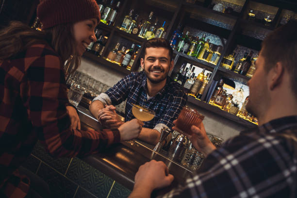 istock Young bartender standing at bar counter with visitors drinking alcohol talking joyful 1165956499