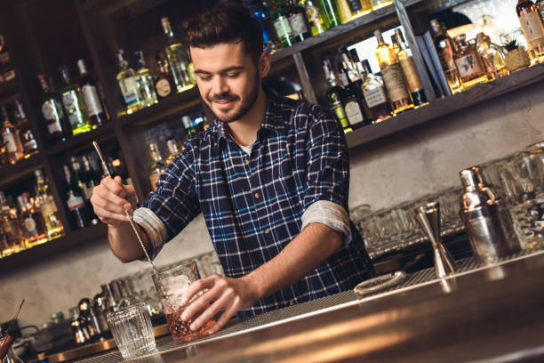 istock Young bartender standing at bar counter mixing cocktail with bar spoon joyful 1165956537