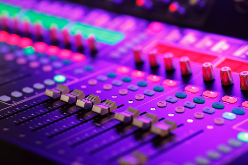 sound mixer with coloured controls and sliders illuminated by stage lights ready for music concert