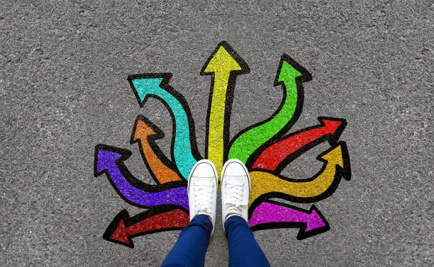 Photo of Feet and arrows on road background. Pair of foot standing on tarmac road with colorful graffiti arrow sign choices