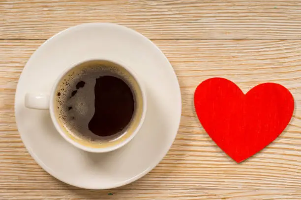 white porcelain cup with hot coffee and red wooden heart shape