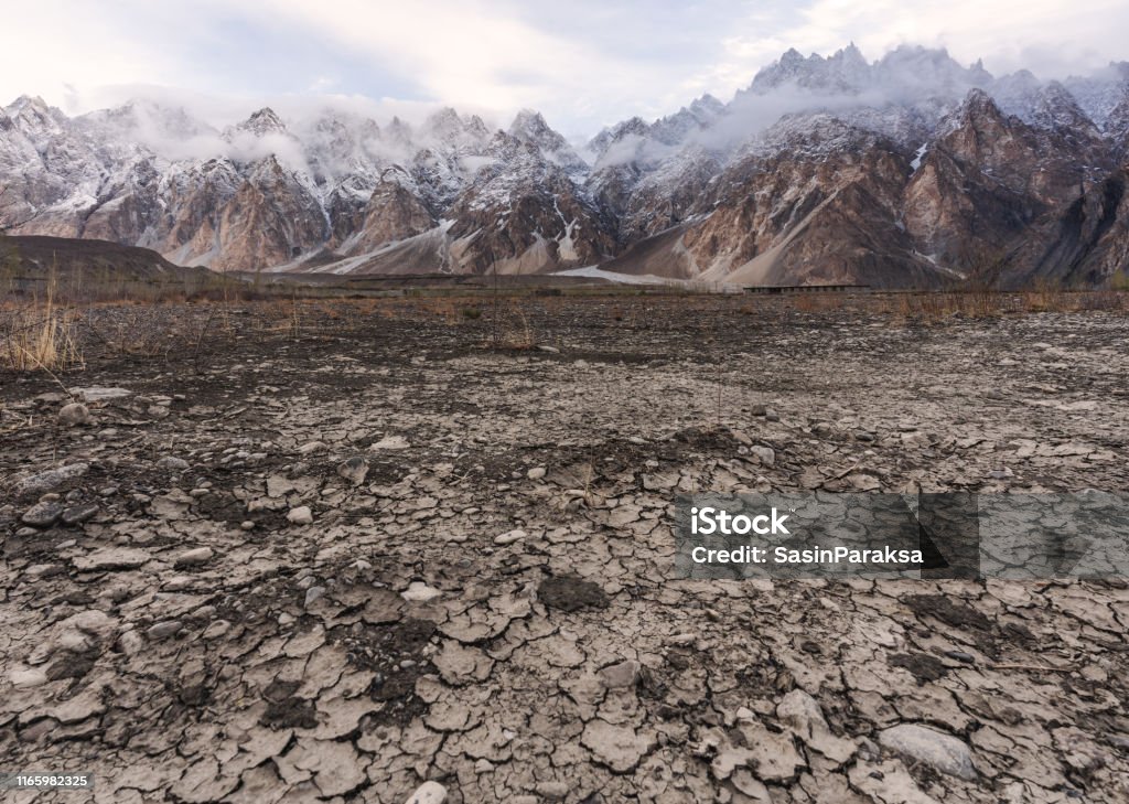 Arid climate, dry cracked drought field with Passu Cathedral mountain landscape in Pakistan Climate Change Stock Photo