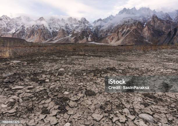 Arid Climate Dry Cracked Drought Field With Passu Cathedral Mountain Landscape In Pakistan Stock Photo - Download Image Now