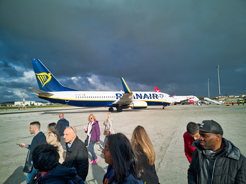 Malta International Airport - April 8 2019:  A medium group of people have disembarked a Ryanair Boeing 737 airplane at Leonardo Da Vinci Fiumicino airport International airport.  Holding luggage and walking towards International Border control for security screening, prior to entering the country.  These security systems were introduced to combat terrorism by the Transport Security Administration.