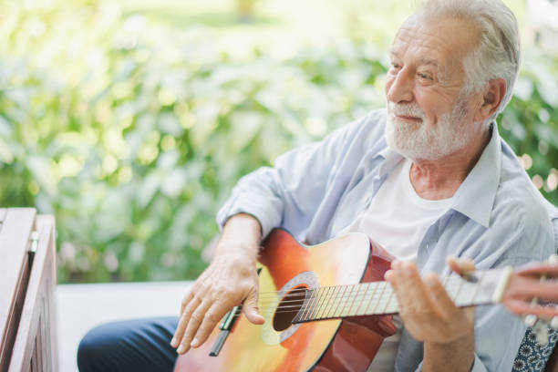 senioren europäische mann spielen eine gitarre im freien grünen garten im altersheim. rentner hase spielt gitarre und lächelt mit felling glücklich. - scherzare stock-fotos und bilder