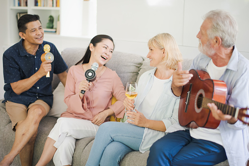 Group of positive seniors European and Asia are singing with playing a guitar at retirement home. Retired people are playing music which fun to enjoying and smiling felling happy.