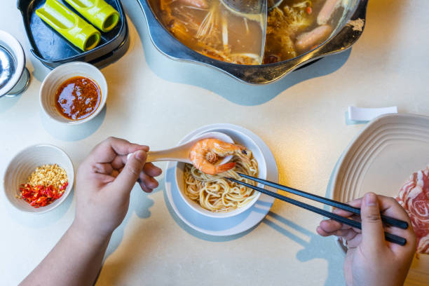 istock Top view of woman hands using chopsticks while eating hotpot 1165995380