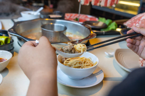 istock Woman hands using chopsticks and spoon while eating hotpot 1165995485