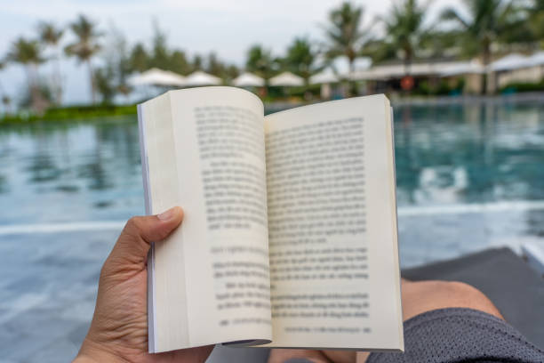 istock Man hand holding a book with swimming pool background 1166000915