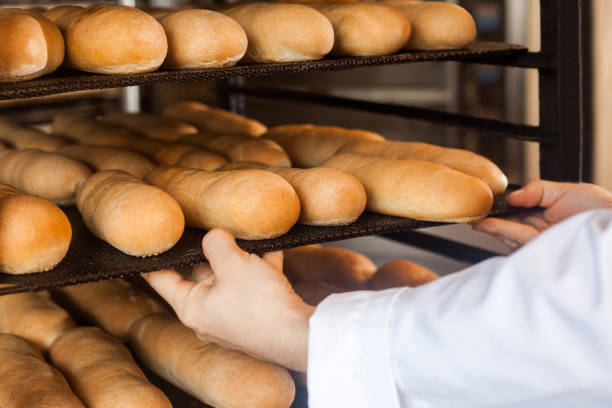 Closeup of hands of professional chef man in white uniform standing near shelves full with fresh bread and pulling baking tray for checking quality Closeup of hands of professional chef man in white uniform standing near shelves full with fresh bread and pulling baking tray for checking quality, Indoor, profession concept filing tray stock pictures, royalty-free photos & images