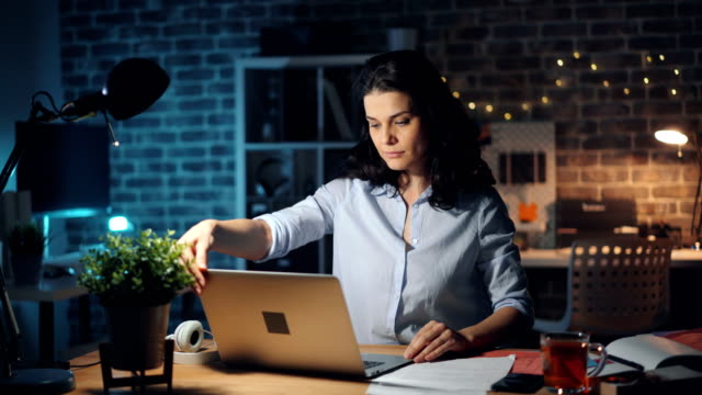 Businesswoman leaving workplace late at night turning off light and laptop