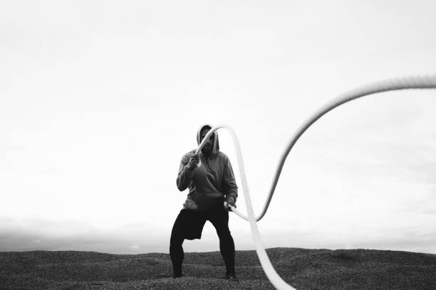 Young athlete training body with two battle ropes on outdoor. Strong man doing intense workout with battle rope at a beach. Black and white color