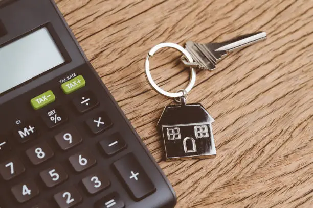 Mortgage calculation or buy and sell house, property and real estate, home key with house keyring or keychain with black calculator on wooden table.
