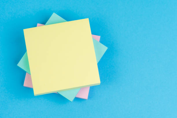 Stack of sticky notes on solid blue background with pink, blue and yellow on top with copy space for writing message using as memo, reminder or business idea and important quote stock photo