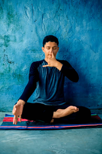 porträtaufnahme des jungen mannes, der pranayama oder pranayam macht oder yoga auf einer bunten matte mit schwarzer kleidung kontrolliert. - prana stock-fotos und bilder