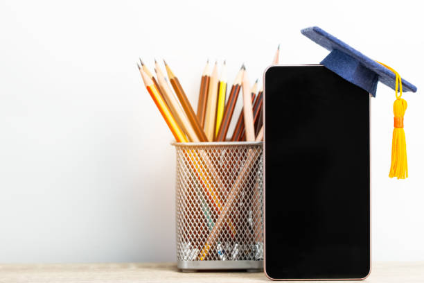 istock Online learning or modern technology study abroad education in global business. Mortarboard graduation cap on blank screen smartphone with pencils on white background. E-learning Graduated in school 1166019121
