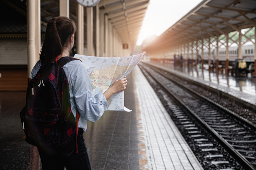 Alone woman with maps and planning travel by train at train station. Alone travel trend 2019 concept.