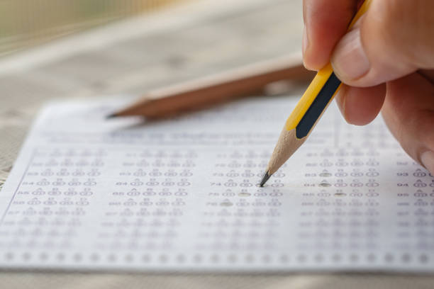 istock Student hand testing doing test exam with pencil drawing selected choices on thai alphabet answer sheets in final exams at college or university. Taking multiple choice for assessment in examination 1166019344
