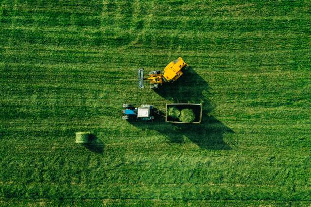 Aerial view of harvest field with tractor moving hay bale Aerial view of green grass harvest field with tractor moving hay bale bale photos stock pictures, royalty-free photos & images