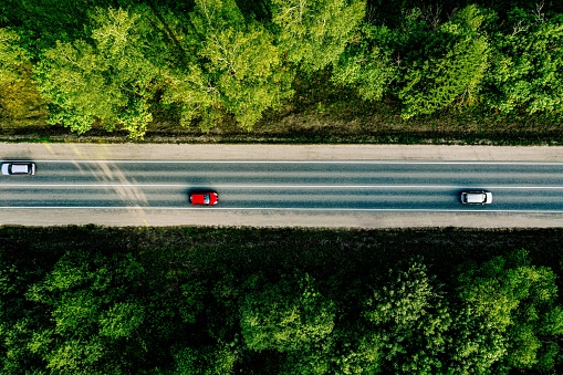 Aerial view of cars driving through the green forest on country road.