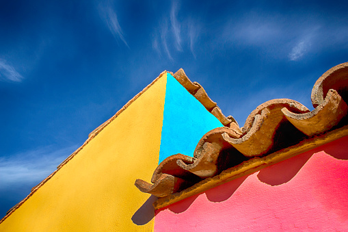 Vividly colored walls and spanish tiled roof set this house apart. The day is bright and beautiful and the sky is blue.  Copy space at the top and left of the image. The image is from Mexico.