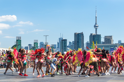 Toronto, Ontario, Canada-August 3, 2019: Motion blur of dancers with the CN Tower in the background.  The Toronto Caribbean Carnival or Caribana is one of the largest street festivals in North America and it attracts thousands of tourists every year leaving about half a million dollars to the economy of Toronto city.