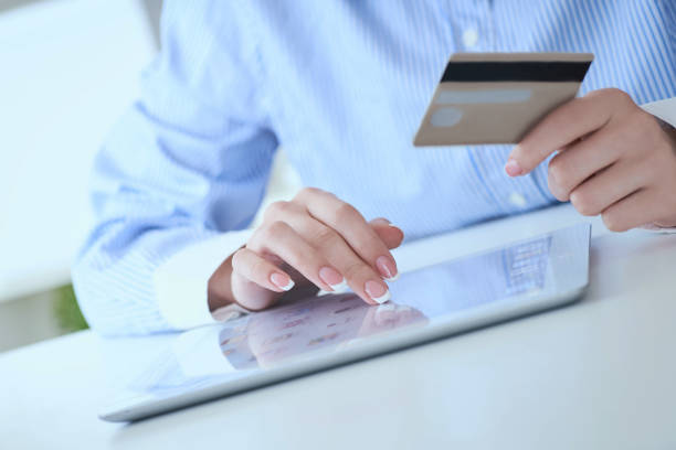 istock Close-up woman's hands holding a credit card and using tablet pc for online shopping. Middle section of young businesswoman making online payments with credit card and tablet. 1166034354