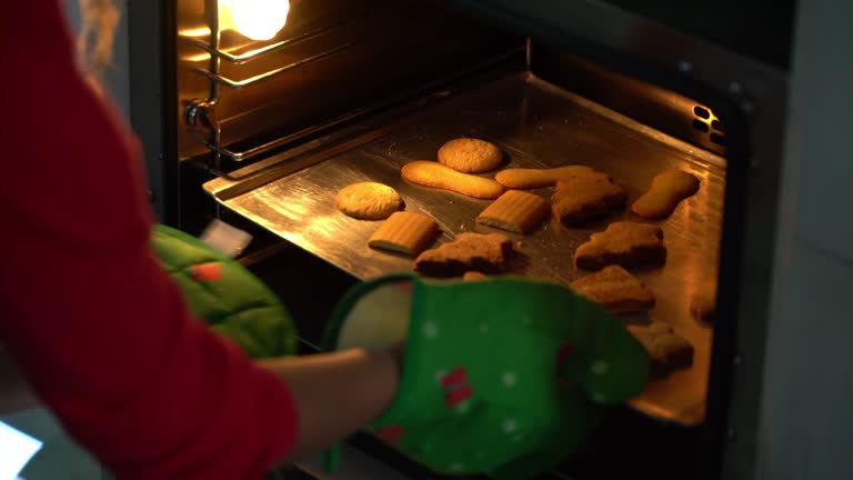 Unrecognizable woman taking out christmas cookies from the oven on tray - Close up