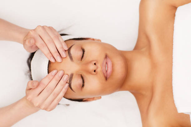 mixed-race woman enjoying face massage in spa - tratamento de estância termal imagens e fotografias de stock