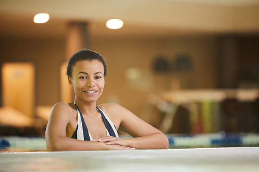 Portrait of beautiful mixed race woman relaxing in swimming pool and smiling at camera, copy space
