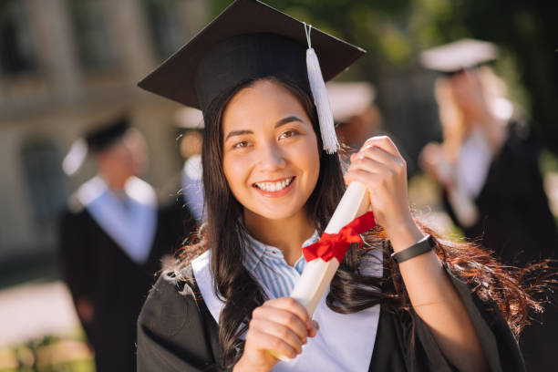 Smiling girl being proud of her masters degree. Worth it. Smiling girl wearing graduation gown holding her diploma with two hands being proud of her masters degree. Master’s Degree stock pictures, royalty-free photos & images