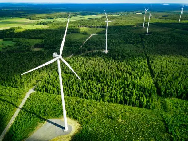Photo of Aerial view of windmills in summer forest in Finland. Wind turbines for electric power with clean and Renewable Energy