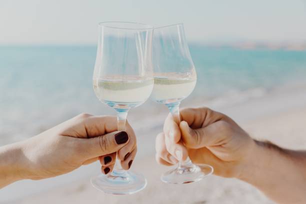 istock Two hands holding glasses with white wine on sea background in Italy. 1166044131