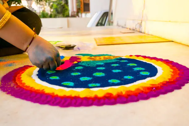 Hand of young indian girl making rangoli from colored powder on diwali eve. These beautiful designs are made in every hindu home to decorate and celebrate the coming of the festivals of diwali, dussera, teej and others