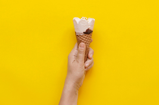 Woman hand holding an ice cream on yellow background