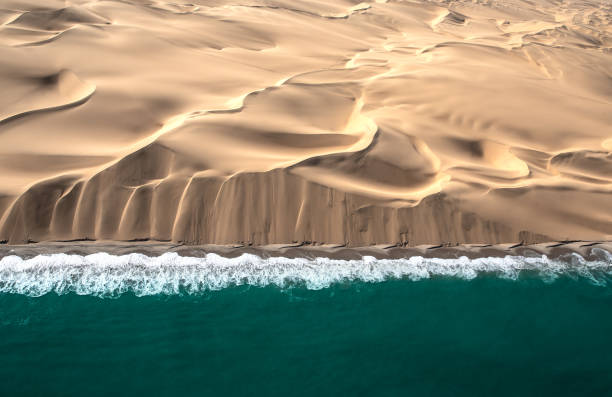 Aerial view of Skeleton coast dunes meeting Atlanic ocean. Aerial view of Skeleton coast sand dunes meeting the waves of Atlanic ocean. Skeleton coast, Namibia. namibia photos stock pictures, royalty-free photos & images