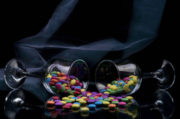 Three champage flute glasses filled with multi coloured generic sugar-coated candies and isolated on black background with reflection
